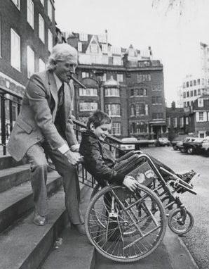 1980年1月23日，萨维尔帮助一名在英国斯托克曼德维尔医院接受治疗的儿童上台阶。萨维尔每年为该医院募集数百万英镑的捐款，但这家医院也是他的性侵场所之一