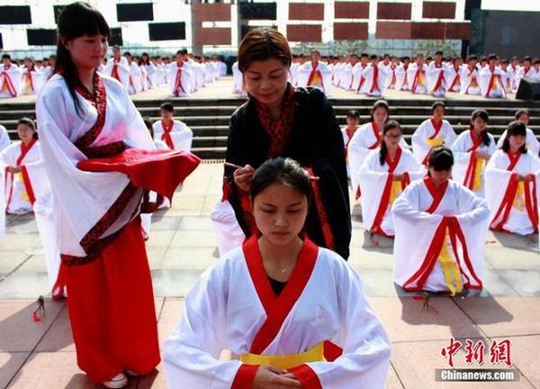 2015年4月21日,湖南省洪江市千名14-24周岁的年轻女子,身穿传统服装,队列整齐,依照古时习俗庄严宣誓,体验成人大典。图为德高望重的长辈为部分女子束起发髻。(图片来源:中新网)